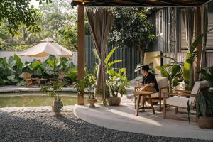 a man sitting in a chair under an umbrella next to a pool at Modapick Bạch Đằng - Living in the nature garden with full river view in Hanoi
