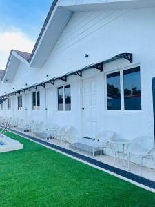 a white building with white chairs and tables and green grass at Impiani Chalet with Private Pool in Kuala Terengganu