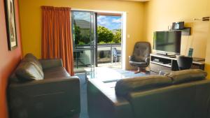 uma sala de estar com 2 sofás e uma televisão e uma varanda em Randolph Motel Apartments em Christchurch