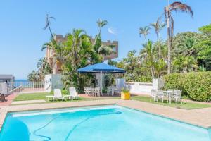 a swimming pool with chairs and a blue umbrella at Club 10 Management in Ballito