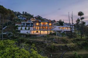a large house on a hill with its lights on at SaffronStays Brookside Estate in Rānīkhet