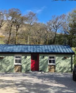 a green building with a red door and a solar roof at Waterfall Cottage in Killybegs