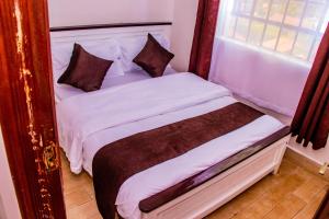 a bedroom with a bed with white sheets and brown pillows at Makenahluxuries Embu Paradise Apartment near Java Gakwegori in Kangaru