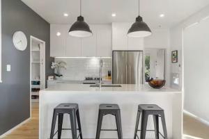 a kitchen with a white counter with three bar stools at Ocean view Designer Standalone Villa Big Deck in Auckland