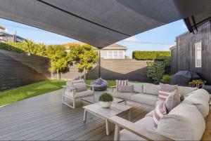 a patio with a couch and chairs on a wooden deck at Ocean view Designer Standalone Villa Big Deck in Auckland