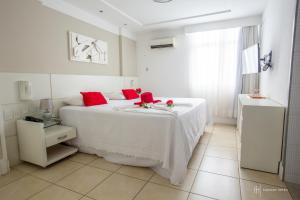 a bedroom with a white bed with red pillows at Rede Andrade Itabuna in Itabuna
