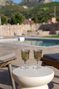 two glasses of wine on a table next to a pool at Vedema Homes in Lefkogeia