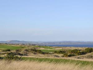 a view of a golf course with the ocean in the background at Dothan Farm Cottage in Cardenden