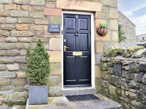 a black door on a stone building with a plant at Quill Corner in Alnwick