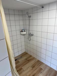 a shower in a white tiled bathroom with a wooden floor at Duna Liget in Dunaföldvár