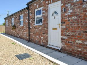 a brick building with a white door and a sidewalk at Dotterel Cottage - Uk39264 in Reighton
