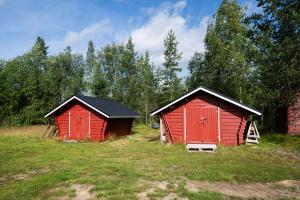 two red buildings in a field with trees at Poromoision pirtti in Peurasuvanto
