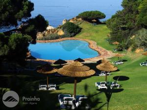 a swimming pool with umbrellas and chairs and the ocean at Aldeamento Turistico da Prainha in Alvor