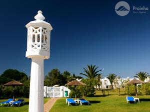 a white clock tower with chairs and umbrellas at Prainha Clube in Alvor