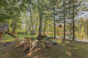 a backyard with two chairs and a grill and trees at Riverfront Getaway with Hot Tub and Scenic Views in Mont-Tremblant