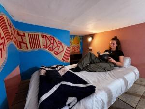 a woman sitting on a bed reading a book at Lienzo Hostal Popayán in Popayan