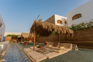 a patio with a straw umbrella and couches and chairs at Home Hotel Dahab in Dahab