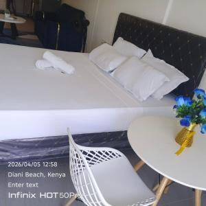 a white bed with a table and a white chair at See breeze sweets villa in Diani Beach