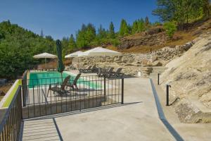 a pool with chairs and umbrellas next to at Riverside Lodges - Serra da Estrela - Chão da Ribeira in Gouveia