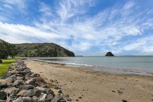 a beach with rocks and the ocean on a cloudy day at Waiwera Beach GetAway in Waiwera