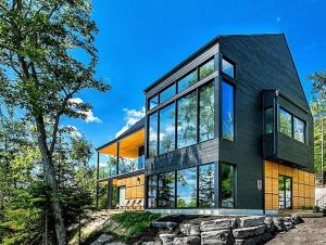 a black house with glass windows and a tree at Secret Charlevoix - River View & Spa in Les Éboulements