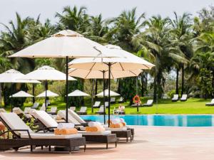 a resort pool with lounge chairs and umbrellas at Mövenpick Ambassador Hotel Accra in Accra