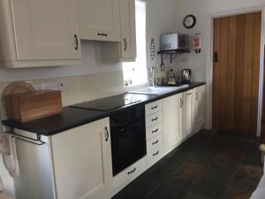 uma cozinha com armários brancos e uma máquina de lavar louça preta em Brookvale Cottage em Downpatrick
