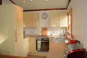 a kitchen with white cabinets and a clock on the wall at Cockleshell Lodge in Otter Ferry