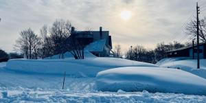 a group of snow covered houses with the sun in the background at Momo Lodge Madarao in Iiyama