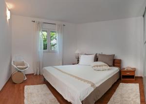 a white bedroom with a large bed and a window at Apartman Roza in Rogoznica