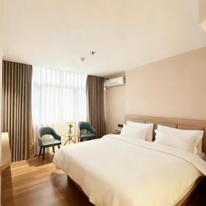 a bedroom with a large white bed and two chairs at Shenzhen Green Oasis Hotel, Baoan in Bao'an