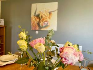 a vase of flowers on a table with a cow painting at Redroofs Barn - 28184 in Weston