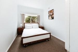a white bedroom with a bed and a window at Iconic Escape Nowra in Nowra