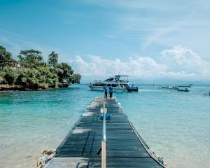 two people standing on a dock in the water with a boat at The Tanis Beach Resort Nusa Lembongan in Nusa Lembongan