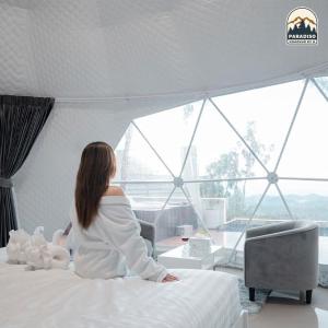 a woman sitting on a bed looking out a window at Paradiso Khaokho By N in Ban Huai Phai