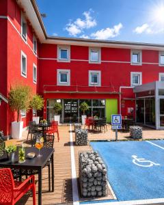 a red building with tables and chairs in front of it at Enzo Hotels Reims Tinqueux in Reims