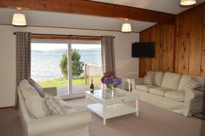 ein Wohnzimmer mit einem Sofa, einem Tisch und einem Fenster in der Unterkunft Cockleshell Lodge in Otter Ferry