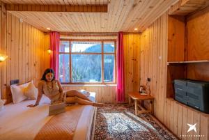 a woman sitting on a bed in a room with a laptop at Zostel Homes Gadagushaini, Jibhi in Jibhi