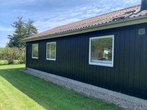 a black house with two windows on the side of it at Beautiful bright summer cottage in Skovbyballe