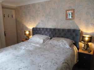 a bedroom with a bed with a blue headboard and two lamps at Marley Farm Bungalow in Deal