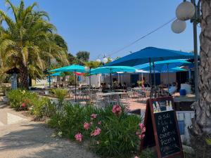 a patio with tables and chairs with blue umbrellas at Le Camping de la Plage in Aregno