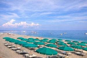 a beach with green umbrellas and chairs and the ocean at Ciao Ciao Rooms in Letojanni