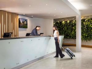 a woman with a suitcase walking past a counter in a lobby at Novotel Auckland Ellerslie in Auckland
