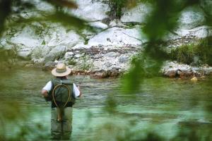 a man in a hat standing in a river fishing at Hotel Hvala Superior - Topli Val in Kobarid