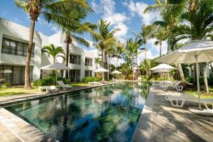 a swimming pool with palm trees and umbrellas at Chic poolside haven 3BR steps from the beach in Cap Malheureux