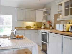 a kitchen with white cabinets and a table with a plate of bread at The Old School House Cottage in Coupar Angus