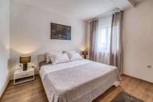 a white bedroom with a bed and a window at Apartments Celebrini in Malinska