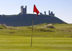 a red flag on a golf course with a castle in the background at The Cottage Inn in Craster