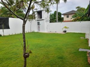 a green yard with a white wall and a tree at Avona Villa in Bopitiya
