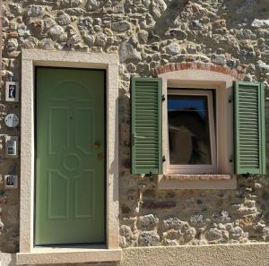 a stone building with a green door and two windows at Cà del Bosco Appartamento Castagno in Il Romito